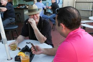 Two men laugh as they smoke cigars and drink whiskey and beer on the patio at Sam's Place Tavern's Cigar Night event