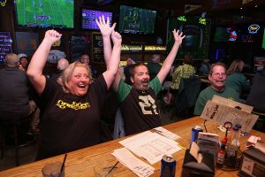 Sam's Place patrons raise their hands excitedly at the bar as the Oregon Ducks make a touchdown